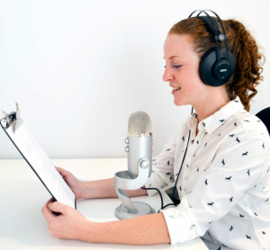 Woman creating voiceover wearing headphones and looking at script.